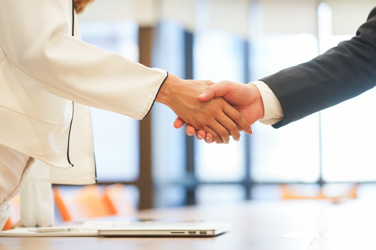 Two people shaking hands next to a laptop