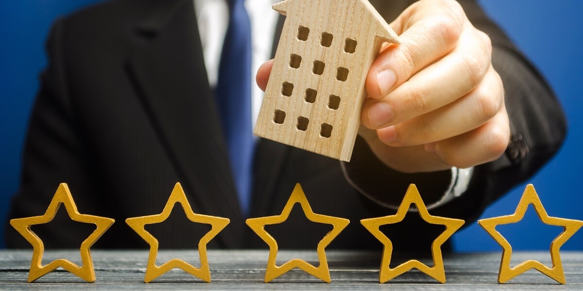 Businessman holding a wooden house next to 5 stars