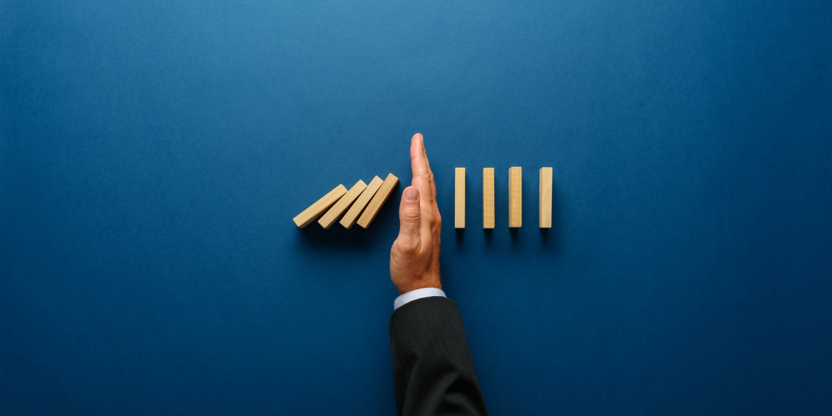 09 Top view of businessman hand stopping falling dominos in a business crisis management conceptual image